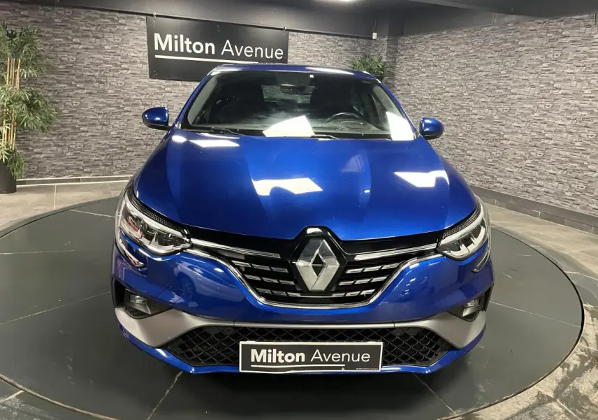 Vue frontale d'une Renault Mégane bleu Iron avec calandre chromée et phares LED en intérieur showroom.