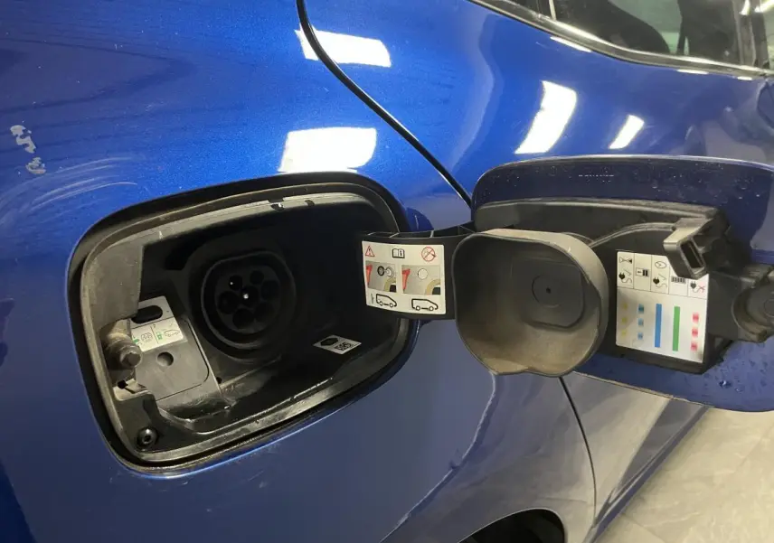 Prise de recharge ouverte côté gauche sur Renault Mégane hybride rechargeable bleu Iron, détails des consignes visibles.