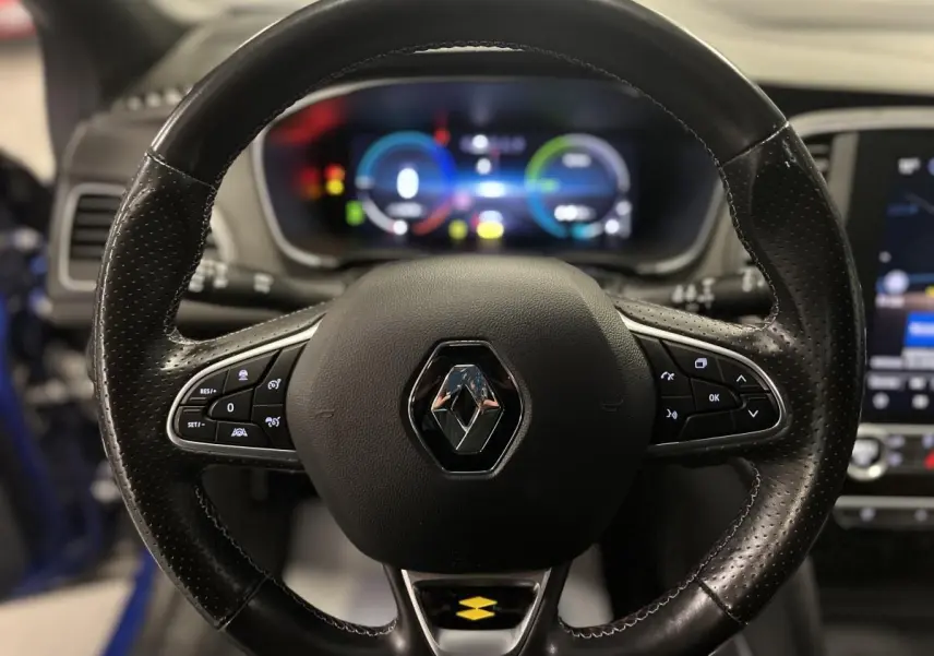 Volant cuir perforé Renault Mégane 1.6 E-Tech bleu, avec commandes intégrées et tableau de bord numérique flou en arrière-plan.