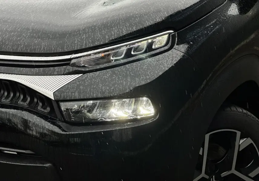 Gros plan sur l'avant droit noir Perla du Citroën C3 Aircross 2024 avec phares LED allumés et jante alliage 17'' distinctive.