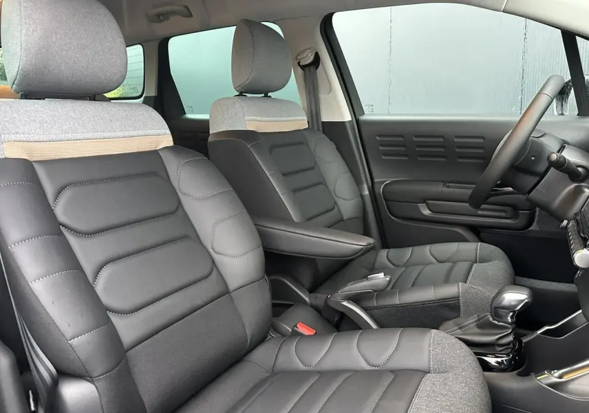 Intérieur de Citroën C3 Aircross 2024, vue côté droit sur sièges mixtes cuir et tissu gris avec accoudoir central.