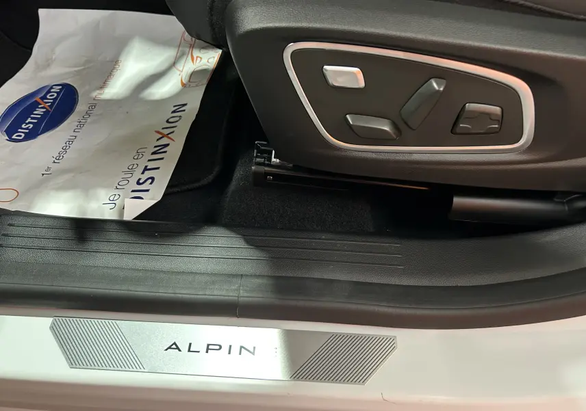 Gros plan sur les commandes électriques du siège côté conducteur et seuil de porte blanc nacré avec logo ALPINE.