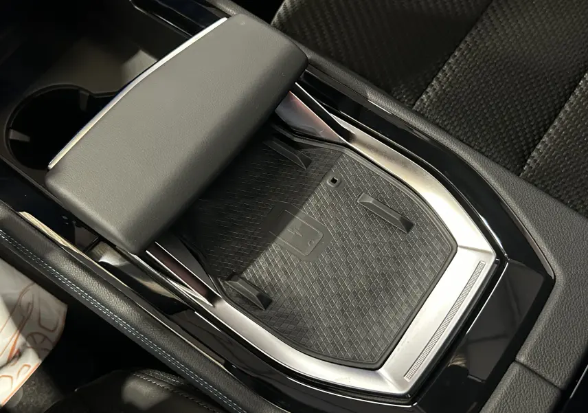 Gros plan sur la console centrale noire du Renault Austral Ph.2 avec surface de charge sans fil et accoudoir cuir.