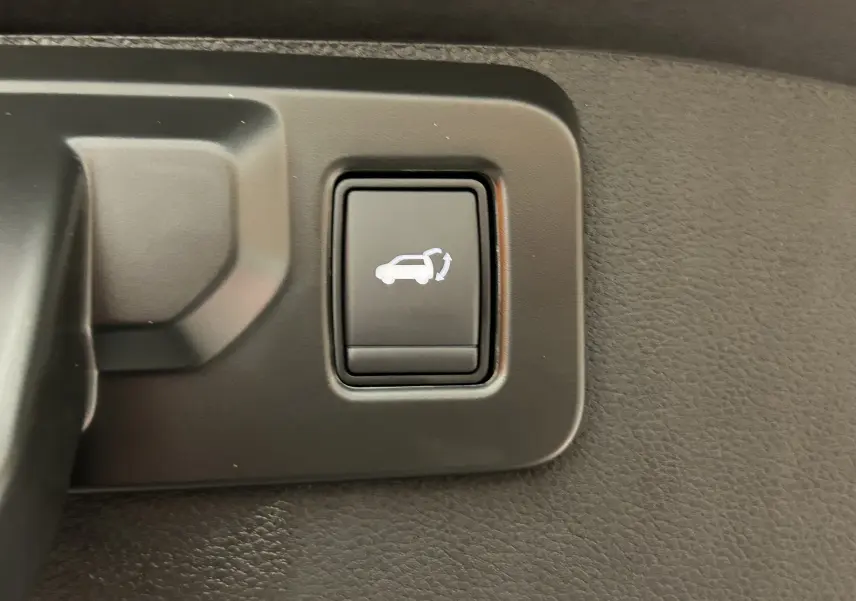 Bouton intérieur noir avec symbole blanc d'ouverture du hayon sur Renault Austral blanc nacré, vue rapprochée.