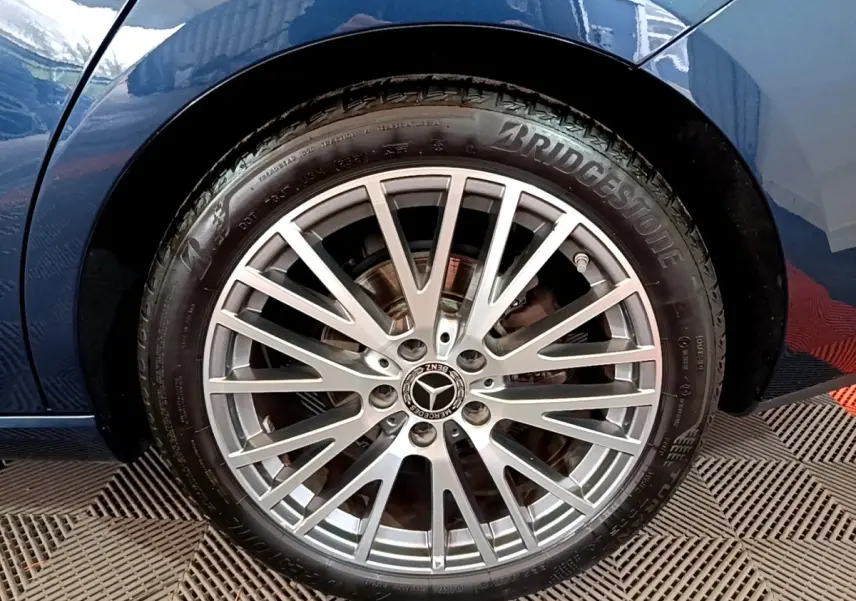 Gros plan sur la jante alu multi-branches argentée et pneu Bridgestone d'une Mercedes CLA 180 d Business Line bleu foncé, côté arrière.