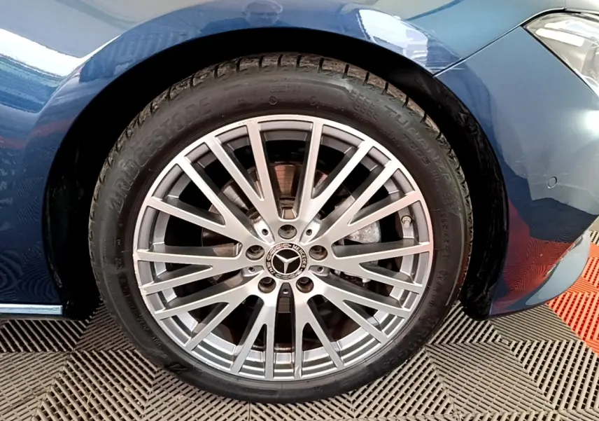 Gros plan sur la jante alu argentée et pneu Bridgestone d'une Mercedes CLA 180 d Business Line bleu foncé, côté avant droit.
