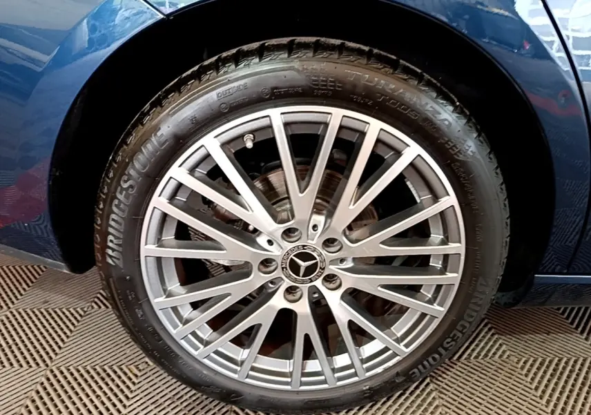 Gros plan sur la jante alu multi-branches argentée d’une Mercedes CLA 180 d Business Line, carrosserie bleu foncé visible.