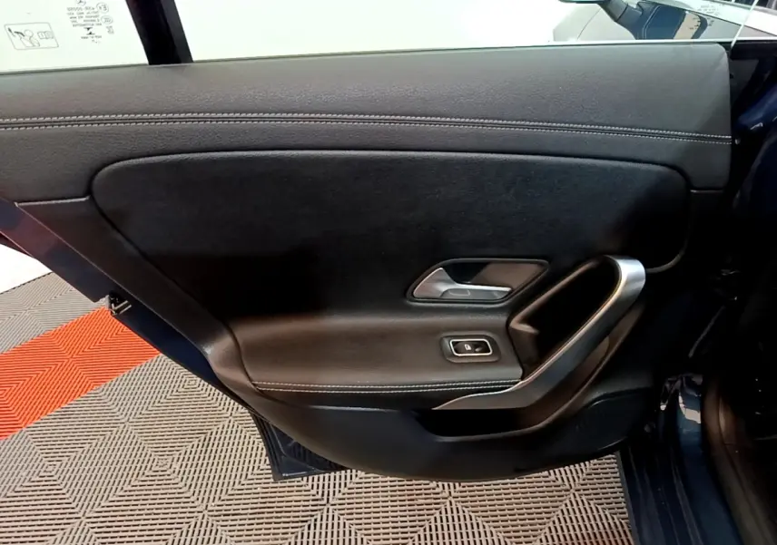 Vue intérieure de la porte arrière gauche noire de la Mercedes CLA 180 d Business Line 2021 avec poignée alu et commande de fenêtre.