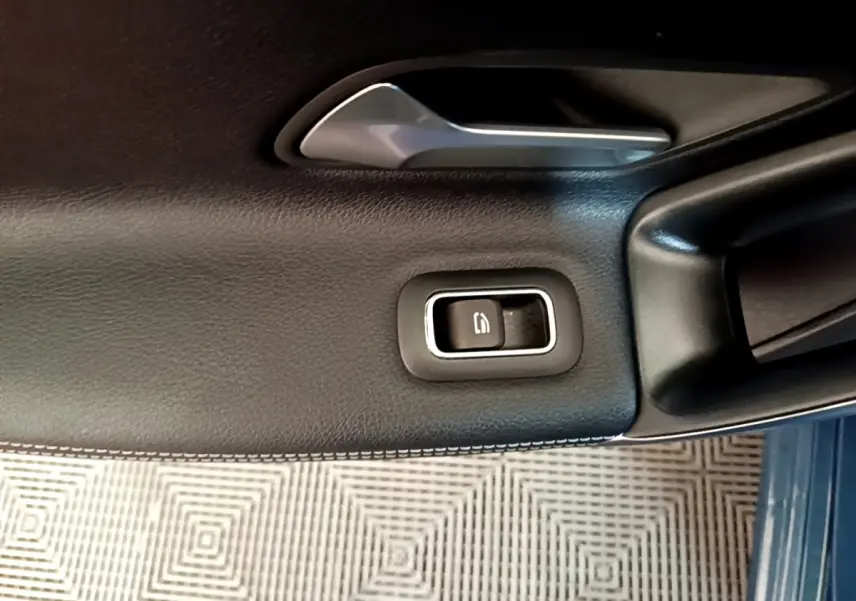 Gros plan sur la commande de lève-vitre côté conducteur en cuir noir avec surpiqûres blanches dans une Mercedes CLA 180 d blanche.