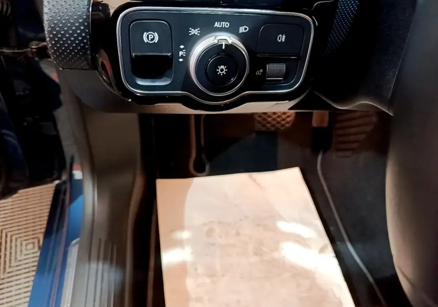 Gros plan sur le panneau de commande des phares et frein à main électrique dans l'habitacle d'une Mercedes CLA 180 d blanche.