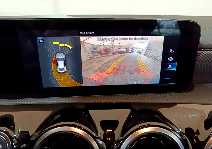 Écran tactile intérieur montrant la caméra de recul et l’aide au stationnement du Mercedes CLA 180 d blanc.