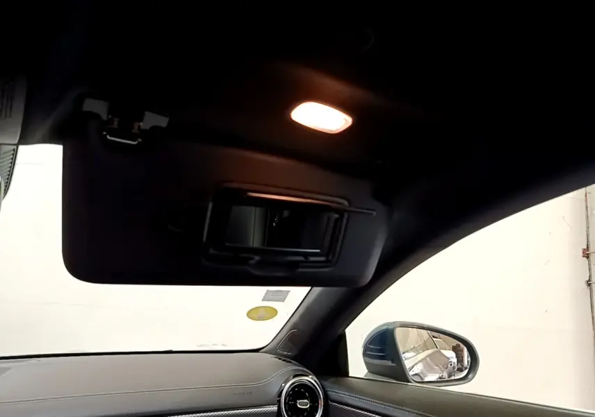 Détail de l'intérieur côté passager d'une Mercedes CLA 180 d Business Line blanche, avec pare-soleil et miroir éclairé.