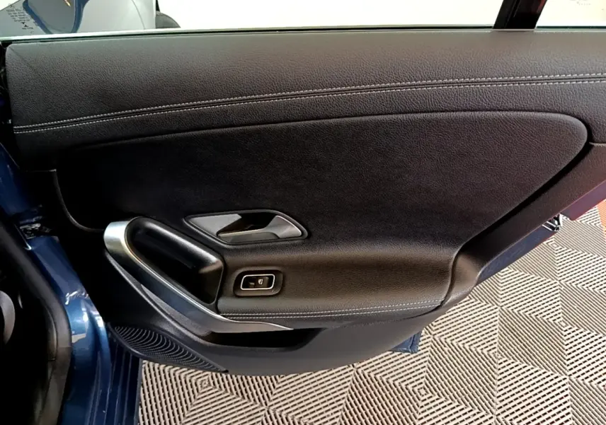 Gros plan sur la porte intérieure côté gauche d'une Mercedes CLA 180 d Business Line blanche, avec poignée alu et cuir noir.