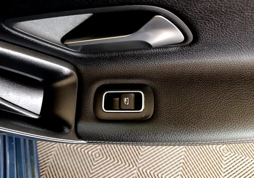 Gros plan sur le bouton de commande de la fermeture électrique de la vitre, sur la porte intérieure noire d’une Mercedes CLA 180 d blanche.