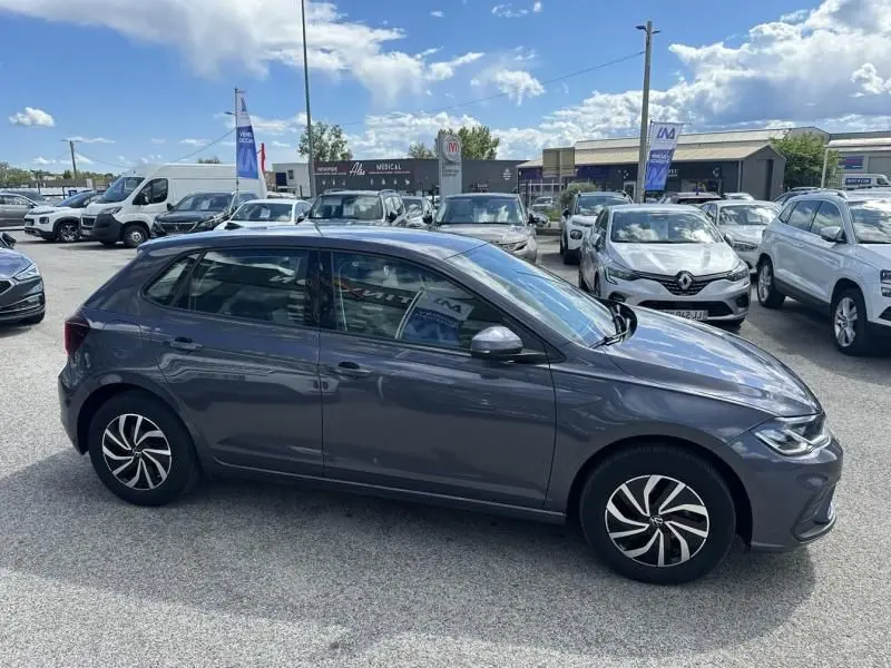 Vue latérale droite d'une Volkswagen Polo 2024 gris foncé métal avec jantes stylisées, stationnée en extérieur sur un parking.