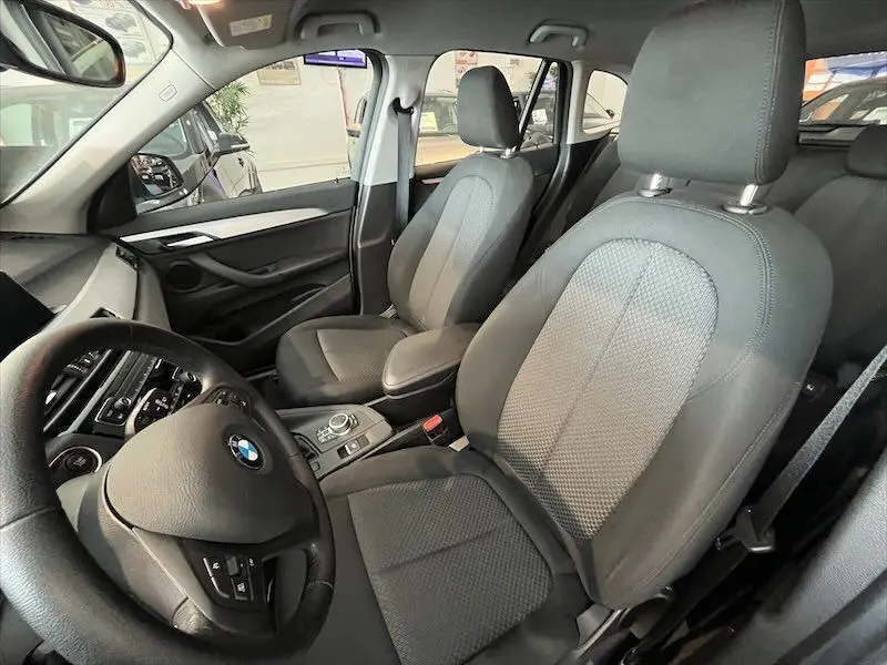 Intérieur avant du BMW X1 25E blanc alpin, vue côté conducteur montrant sièges et tableau de bord noir.