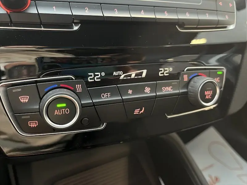 Gros plan sur la console de climatisation digitale du BMW X1 blanc, affichant 22 degrés et réglages automatiques.