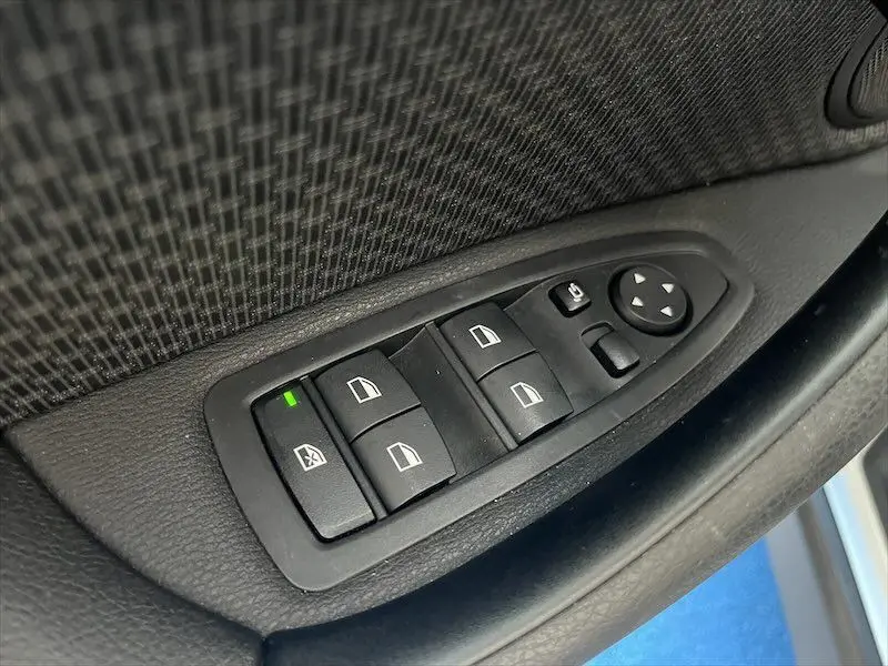 Gros plan sur les commandes de lève-vitres côté conducteur d'une BMW X1 XDRIVE blanche, intérieur noir.