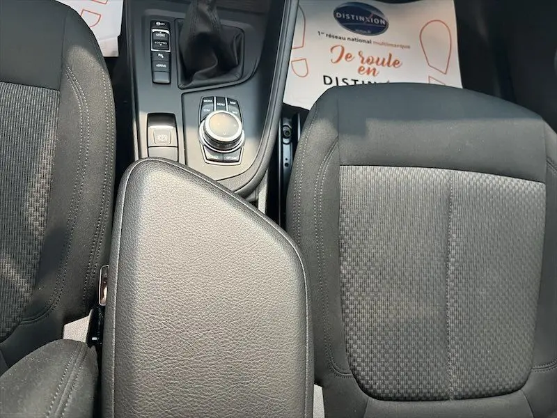 Vue plongeante sur l’intérieur de la BMW X1 XDRIVE 25E, montrant la console centrale et les sièges noirs en tissu.