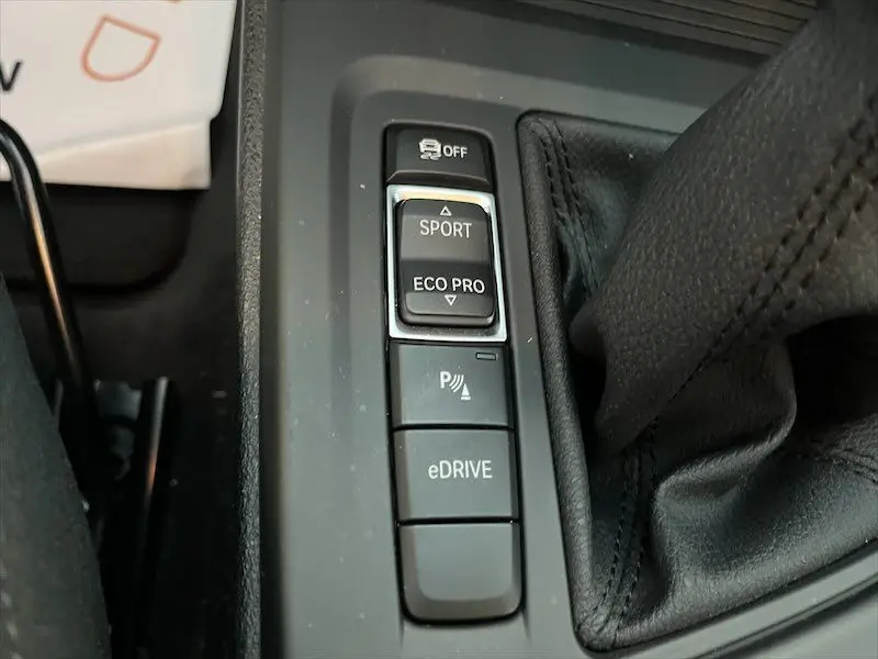 Gros plan sur les boutons de mode de conduite et assistance de la console centrale d'un BMW X1 blanc alpin hybride rechargeable.