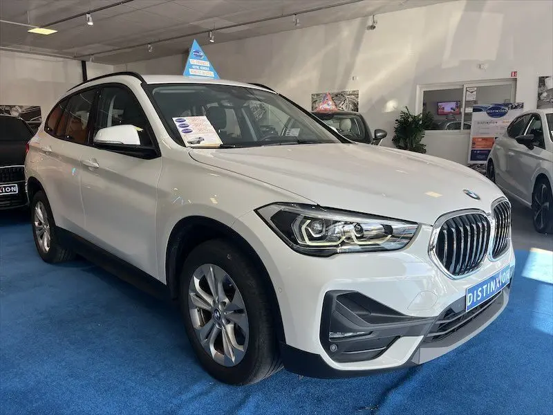 BMW X1 XDRIVE blanc alpin vue 3/4 avant droit en showroom avec calandre et phares LED visibles