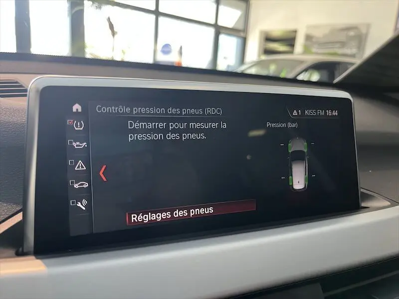 Écran tactile intérieur BMW X1 25E blanc, affichant le contrôle de pression des pneus en mode réglages.