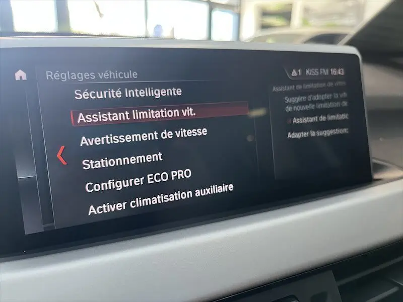 Écran central du BMW X1 25E blanc montrant les réglages de sécurité intelligente et assistant limitation vitesse.