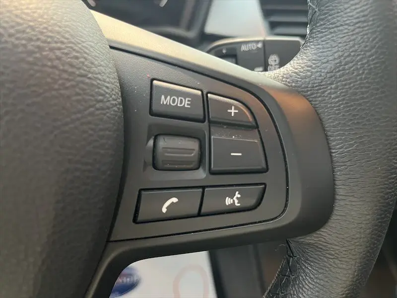 Gros plan sur les commandes du volant à droite du BMW X1 XDRIVE blanc alpin, boutons mode, volume et téléphone.
