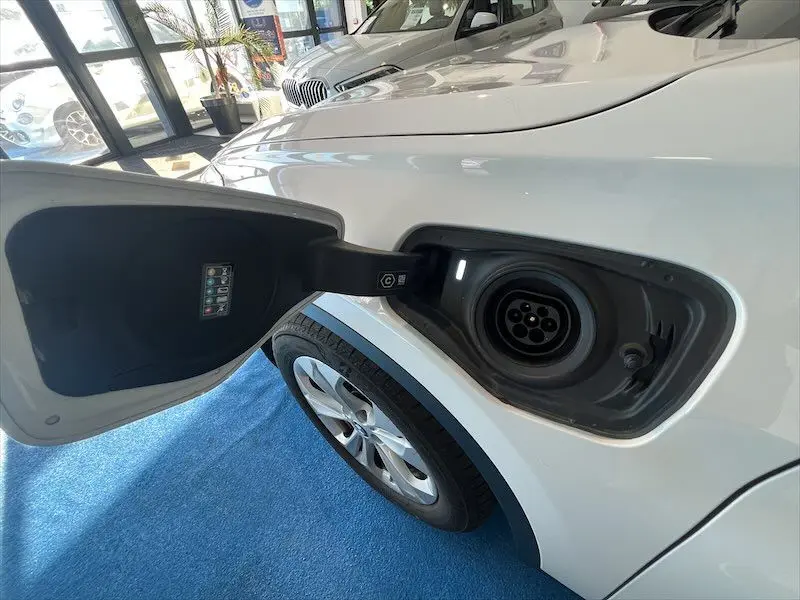 Prise de recharge ouverte côté gauche d'un BMW X1 XDRIVE blanc alpin, montrant la trappe et la roue arrière.