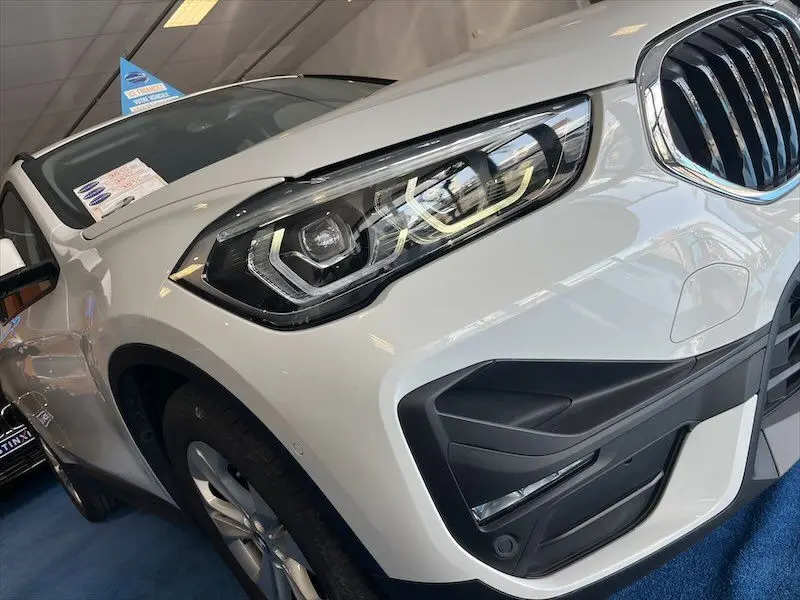 Gros plan sur le phare avant droit du BMW X1 XDRIVE blanc alpin, mettant en valeur la calandre et les détails du pare-chocs.