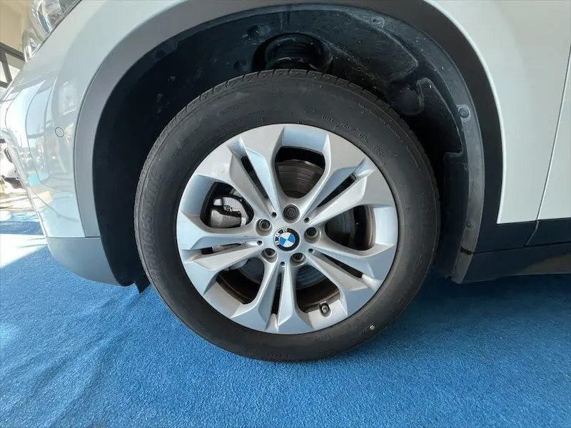 Gros plan sur la roue avant gauche d'un BMW X1 XDRIVE blanc alpin, mettant en valeur la jante en alliage et le logo BMW central.