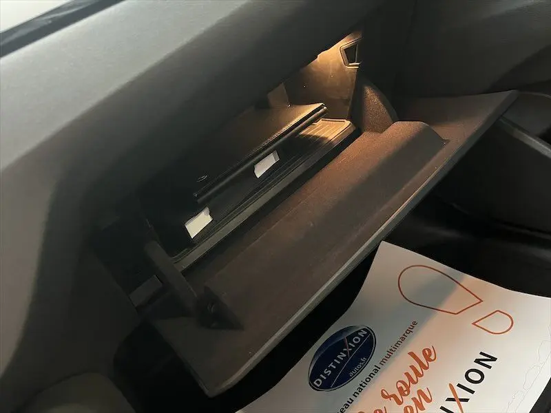 Gros plan sur la boîte à gants ouverte du BMW X1 XDRIVE blanc, montrant l'intérieur et un document Distinxion.