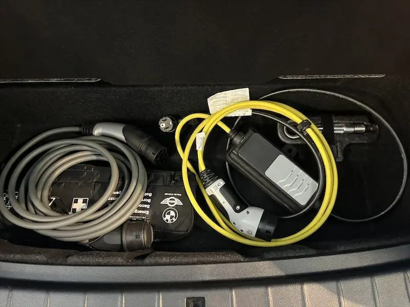 Coffre ouvert d’un BMW X1 blanc avec câbles de recharge hybride rangés, vue plongeante sur le compartiment.