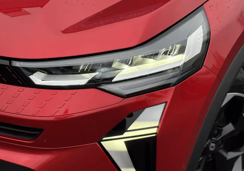 Gros plan sur le phare avant droit du Renault Captur 2025 Rouge Flamme avec détails LED et jante alu noire visible.