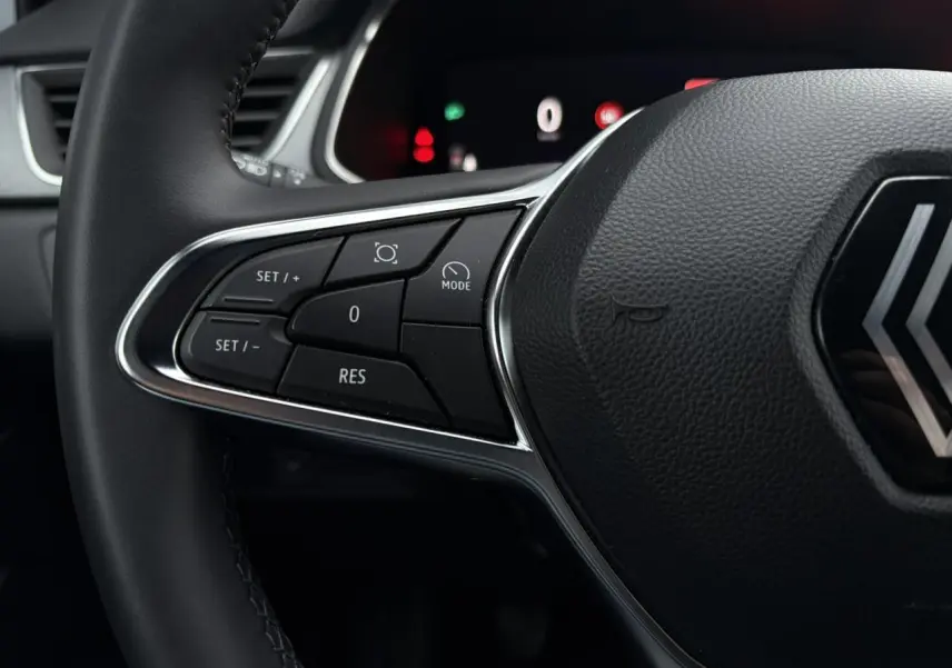 Gros plan sur les commandes à gauche du volant noir du Renault Captur 2025, avec tableau de bord numérique en arrière-plan.