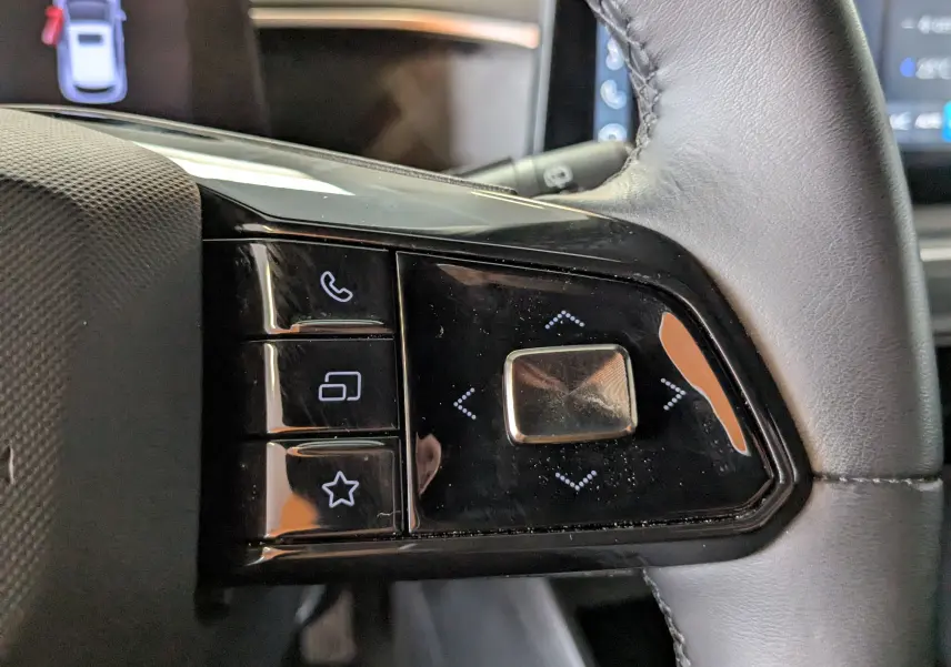 Gros plan sur les commandes noires du volant en cuir de la MG3 1.5 L Hybrid+ 2025, avec boutons tactiles et finition brillante.