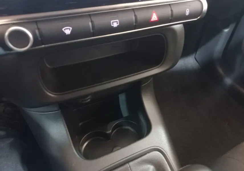 Gros plan sur la console centrale noire de la Citroën C3 2024, avec porte-gobelets et boutons de commande alignés.