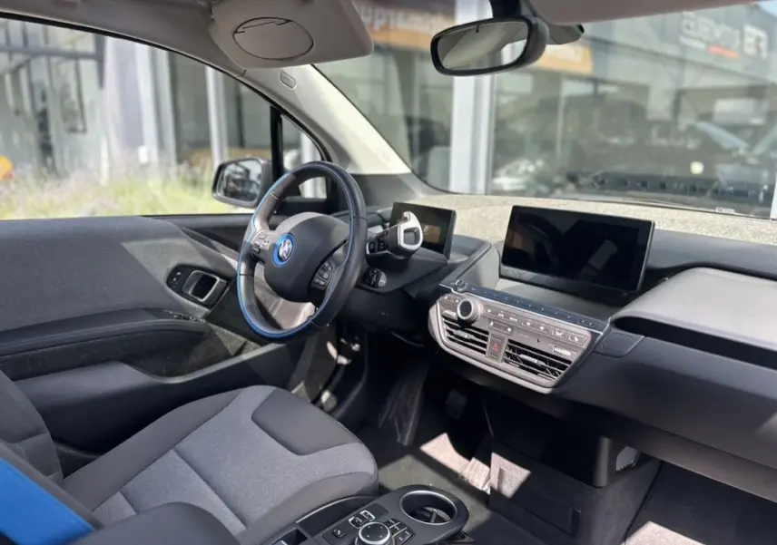 Intérieur de la BMW i3 noire 2022 vu côté conducteur, tableau de bord moderne avec écran tactile et volant multifonction.