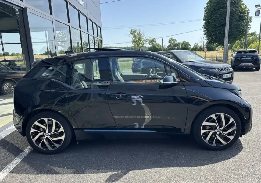 BMW i3 noire vue de profil côté gauche, mettant en valeur ses jantes distinctives et sa silhouette compacte électrique.