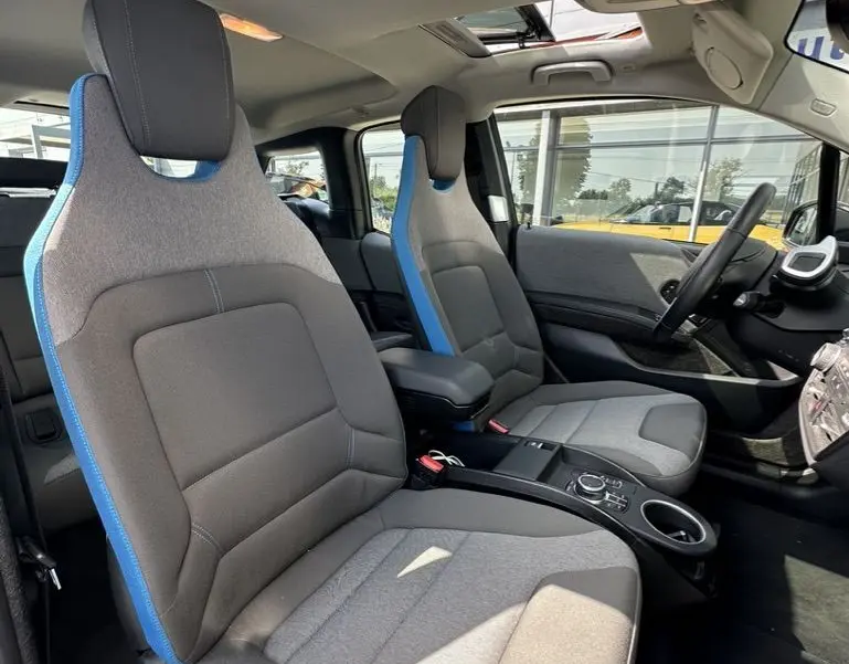 Intérieur de la BMW i3 2022 noir, vue côté droit sur les sièges avant gris avec surpiqûres bleues et toit ouvrant.