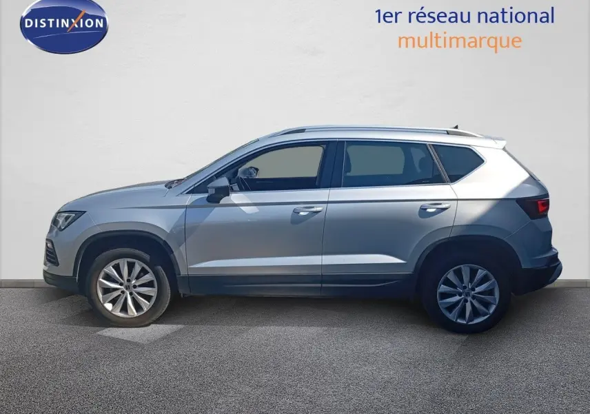 Vue de profil côté gauche d'un SEAT Ateca 2023 argent Reflex Metal avec jantes alliage et toit équipé de barres longitudinales.