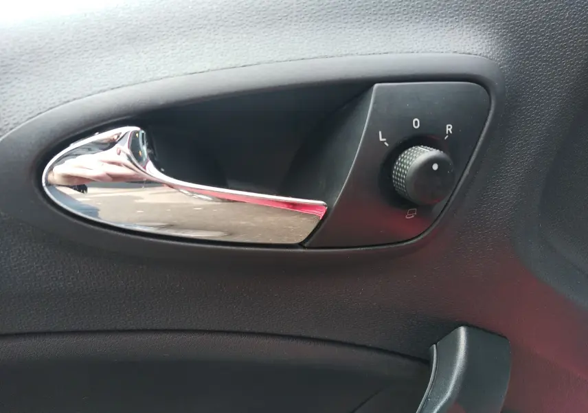 Gros plan sur la poignée intérieure chromée et le réglage des rétroviseurs côté conducteur d'une SEAT Ibiza ST rouge.