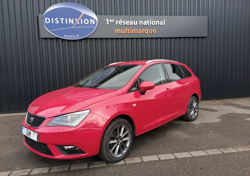 SEAT Ibiza ST rouge vue 3/4 avant droit, avec jantes alliage et phares xénon, stationnée devant un mur noir.
