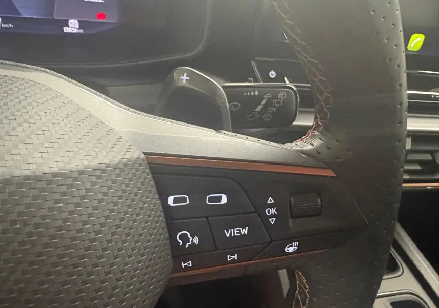 Gros plan sur le volant perforé de la CUPRA Leon blanc Nevada 2024 avec commandes intégrées et palettes au volant.