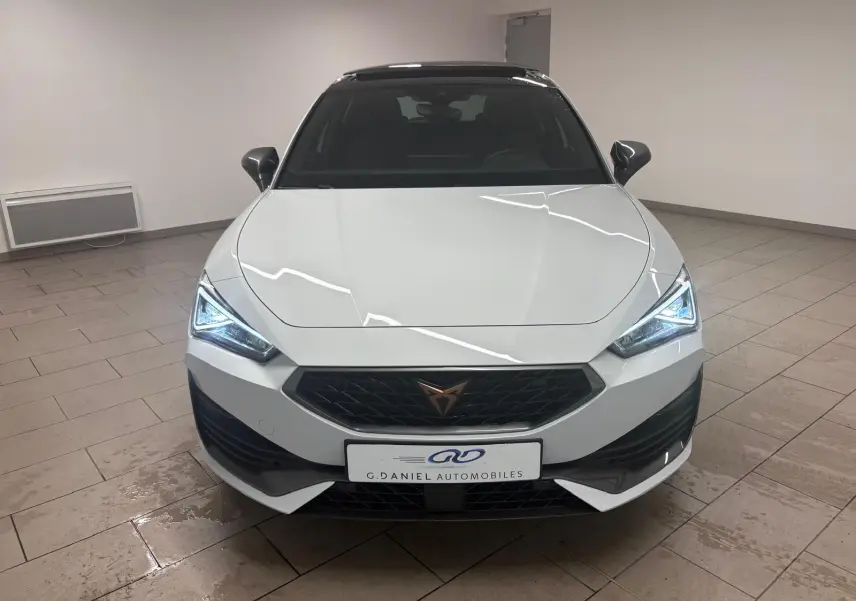 Vue frontale d'une CUPRA Leon blanche Nevada avec toit ouvrant panoramique et phares LED allumés en intérieur.