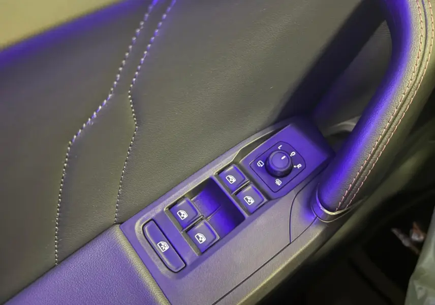 Gros plan sur les commandes des vitres et rétroviseurs côté conducteur, avec surpiqûres rouges sur la garniture noire.