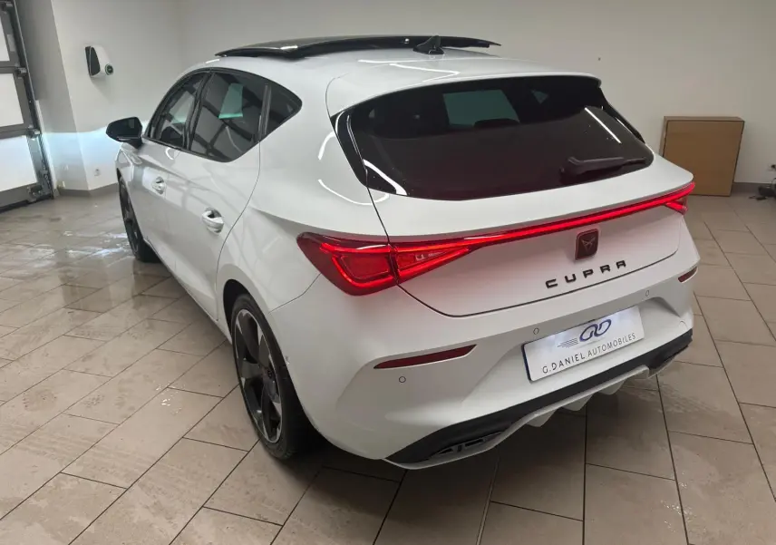 Vue 3/4 arrière droite d'une CUPRA Leon blanche Nevada avec toit ouvrant panoramique et feux arrière allumés.