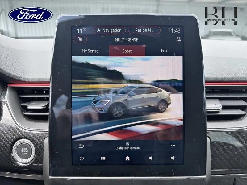 Écran tactile intérieur montrant la Renault Arkana gris métallisé en vue latérale droite dans le mode Sport.