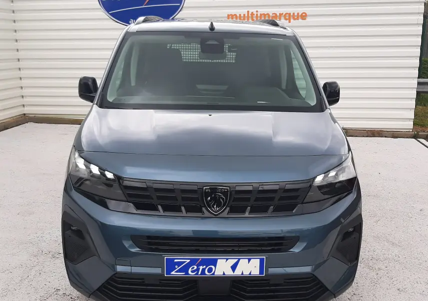 Vue avant d'un Peugeot Rifter 2026 bleu Kiama avec calandre noire et logo lion central, sur parking devant panneau Distinxion.