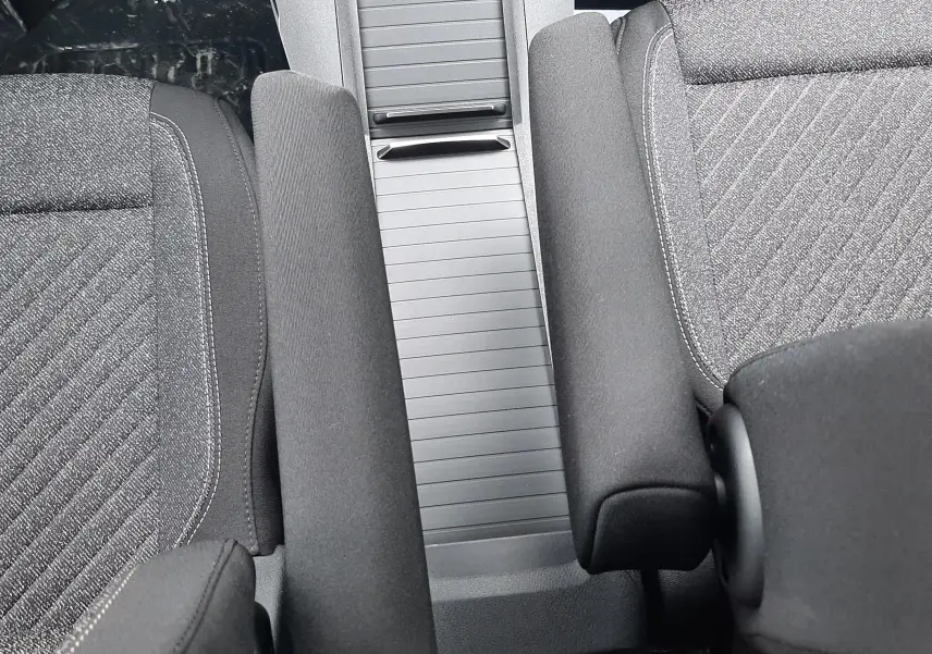 Vue rapprochée de l’intérieur du Peugeot Rifter 2026, montrant la console centrale grise et les accoudoirs noirs entre les sièges tissu gris.